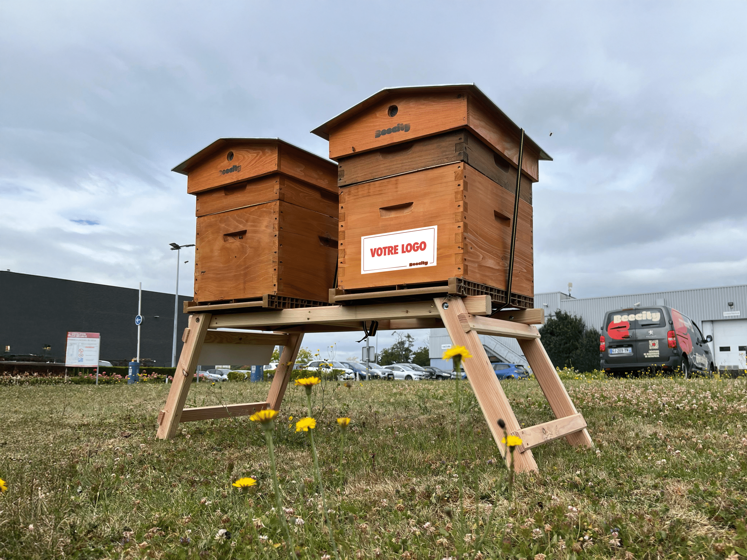 Deux ruches BEECITY sur pieds dans l'espace vert d'une entreprise, l'une portant une plaque « Votre logo »